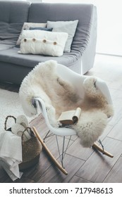 Still Life Details Of Living Room. Sheep Skin Rug On Modern Armchair By The Sofa With Cushions. Reading Book On The Rocket Chair. Cozy Winter Scene In Scandinavian Interior.