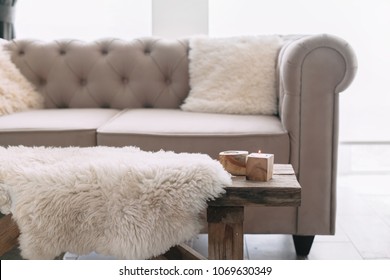 Still Life Details Of Nordic Living Room. Sheep Skin Rug On Rustic Bench By The Sofa With Fur Cushions. Cozy Winter Scene In Scandinavian Interior.