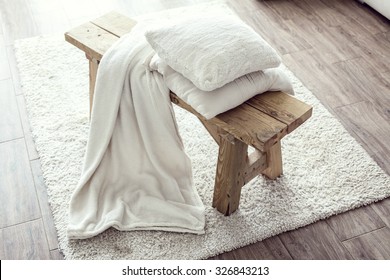 Still life details, stack of white cushions and blanket on rustic bench on white carpet