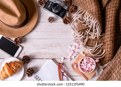 Still life details of travel. Cup of hot cocoa with marshmallows,hat, phone, vintage camera and plaid on the wooden table.