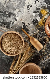 Still Life With Ears Of Golden Wheat, Seeds And Flour In Rustic Wooden Bowl On A Messy Kitchen Table With Copy Space Viewed From Above