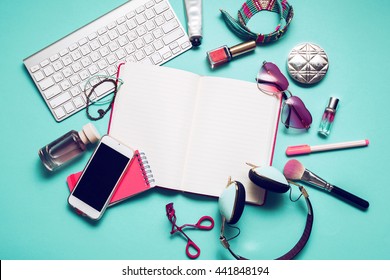 Still life of fashion woman, girl,student on  trendy blue background. Overhead of essentials for modern young person .Note book, nail polish, lipstick,  powder, glasses, watch,  stylish 
headphones.