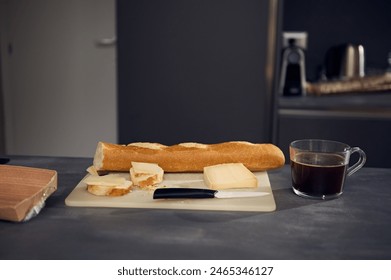 Still life with a fast food lunch on the kitchen table. A cup of freshly brewed espresso coffee near a cutting board with a whole grain baguette, loaf of bread and sliced cheese on the kitchen table - Powered by Shutterstock