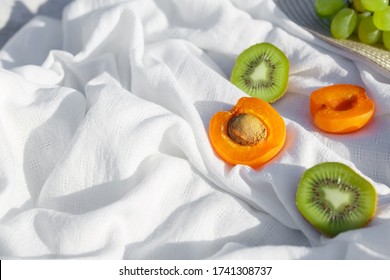 Still Life And Food Photo. Kiwi And Apricot Fruit Lie On A White Wave-crumpled Fabric Under Bright Contrasting Sun Rays