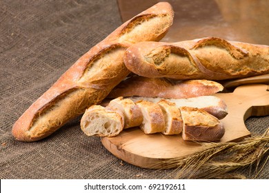 still life with French fresh bread baguettes with poolish on a wooden cutting board and wheat, shallow dof