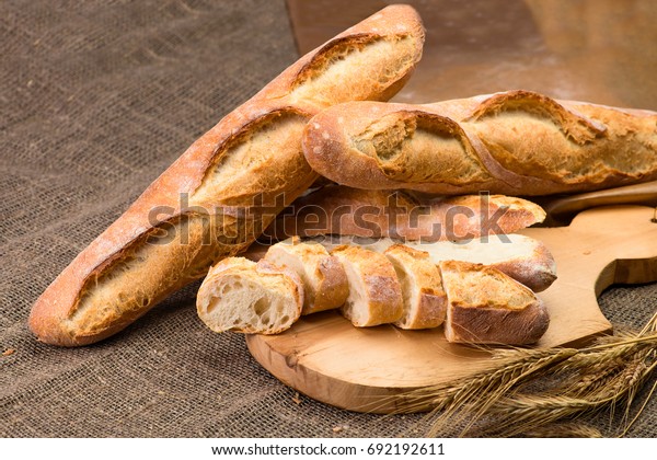 still life with\
French fresh bread baguettes with poolish on a wooden cutting board\
and wheat, shallow dof