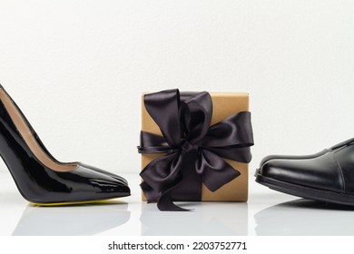 Still Life Of Gift Box With Black Ribbon And Shoes. Classic Black Mens And Womens Footwear Isolated On White.