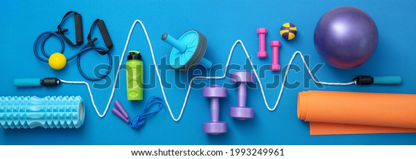 still life of group sports equipment for womens\
and cardiogram of jump rope, on blue background. Fitness and\
healthy living, wellness\
concept.