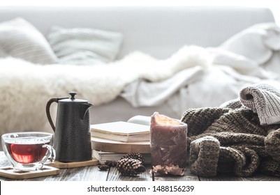 Still Life Home Comfort In The Living Room With A Cup Of Tea And A Kettle , Near A Burning Candle And A Knitted Sweater.The Concept Of Home Atmosphere And Comfort