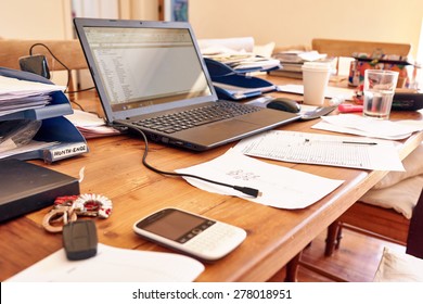 Still Life Images Of A Busy Entrepreneur's Desk In Their Home Office Space, With Technology And Paperwork Cluttering The Table Space