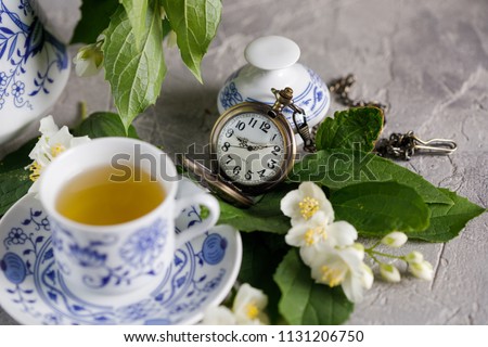 Still life with a magnificent tea set with jasmine flowers and a clock bulb.