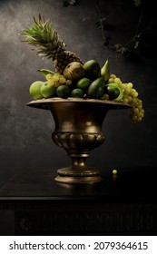 Still Life with many different green fruits in big silver vase. Dark wall background, antique wooden table, pineapple, wine grapes, green apples, limes. Great for designers and interior decoration.  - Shutterstock ID 2079364615