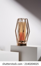 Still Life Photo Of A Golden Candle Holder Made Out Of Gold Metal And Tinted Glass. The Designer Candle Holder Is Located On White Surface Against White Wall.