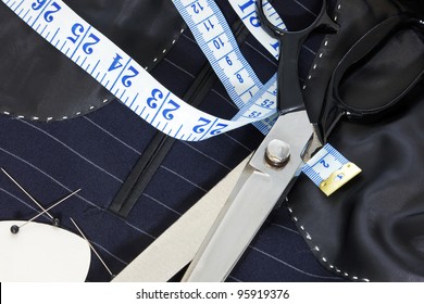 Still life photo of the inside of a bespoke suit jacket with hand stitching and scissors, tape measure, chalk and pins.