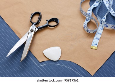 Still life photo of a suit pattern template with tape measure, chalk and scissors.