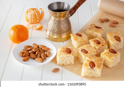 Still life Pieces Basbousa (namoora) traditional arabic semolina cake with almond nut and syrup, orange and cooper jezva. Copy space. Selective focus.