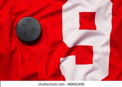 Still Life Puck On A Red And White Number 9 Jersey As A Sport Background. Ice Hockey Season Concept Closeup, Top View.