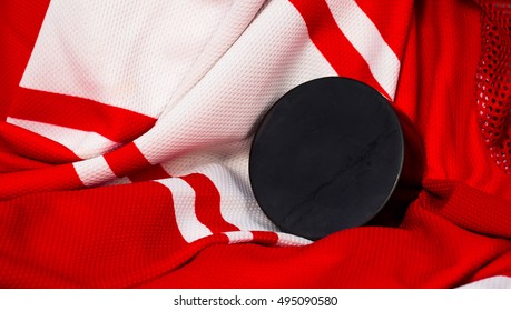 Still life puck on a red and white jersey as a sport background. Ice hockey season concept close up, top view.