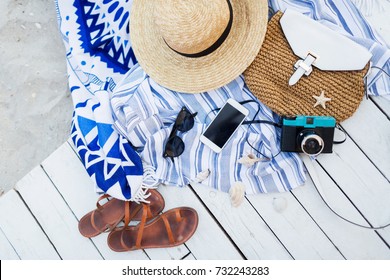 Still life of random objects of modern girl / woman on her summer vacation . Top view on  holiday set  on white wooden background. Straw hat, beach  sandals,   photo camera, sunglasses, mobile phone.