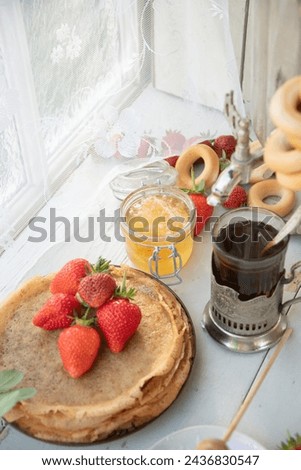 Still life in the Russian tradition for Maslenitsa, pancakes with honey and strawberries, tea in a faceted glass with a silver glass holder with bagels, Slavic holiday, high quality photo