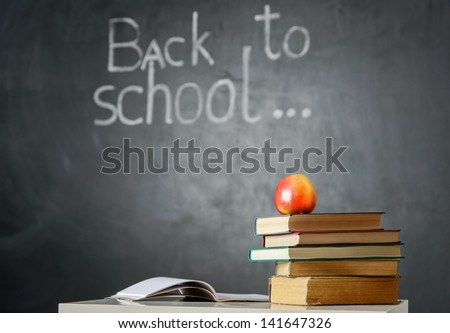 Still life with school books and apple against blackboard with 