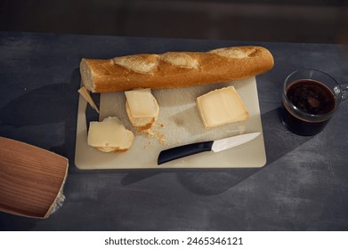 Still life top view breakfast on the kitchen table. A cup of freshly brewed espresso coffee near a cutting board with a whole grain baguette, loaf of bread and sliced cheese on the kitchen table - Powered by Shutterstock