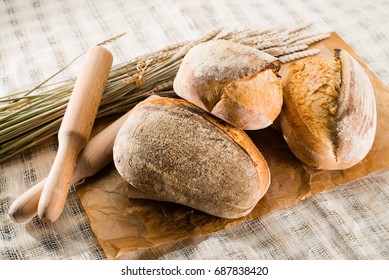 still life with a traditional round artisan wheat bread loaves, wheat and pestles on light textile background, shallow dof - Shutterstock ID 687838420
