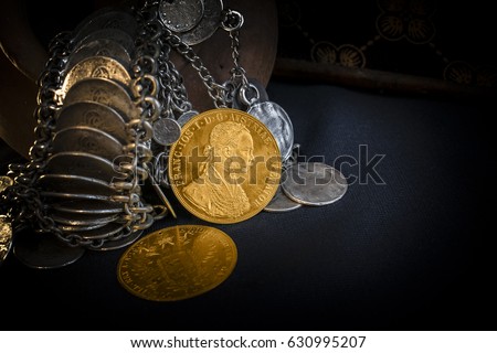 Still Life with two Austria-Hungary thalers, avers and revers of golden coin-ducats from 1915 with Kaiser Franz Joseph I, leaning on silver jewelery and dark environment [[stock_photo]] © 