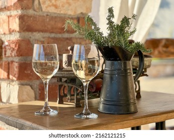 Still Life; Two Wine Glasses On A Table With A Scale In The Background And A Jug Filled With A Herb Plant