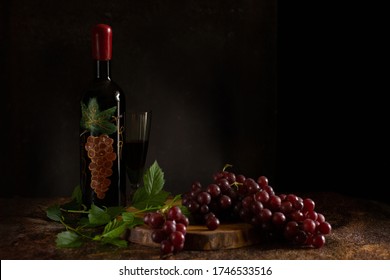 Still life and an unusual bottle wine  and bunch dark grapes   branch   green glass glass red wine dark black background  Beautiful drawing the bottle and paints 
