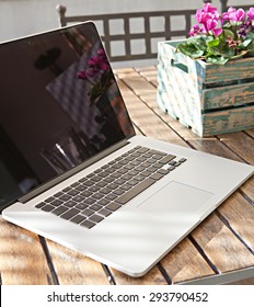 Still Life View Of Open Laptop Computer On A Terrace Patio Wooden Table With Decorative Flower Pot In Home Exterior Area, Outdoors. Technology At Home And Working From Home Environment With No People.