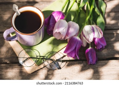 Still Life In Vintage Style. A Fancy Purple Coffee Mug, An Old Book, Glasses And Tulips On A Wooden Table. The Holiday Is March 8. International Women's Day.