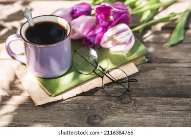 Still Life In Vintage Style. A Fancy Purple Coffee Mug, An Old Book, Glasses And Tulips On A Wooden Table. The Holiday Is March 8. International Women's Day.