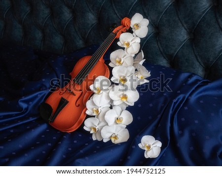 Still life with violin and white orchid on a bed