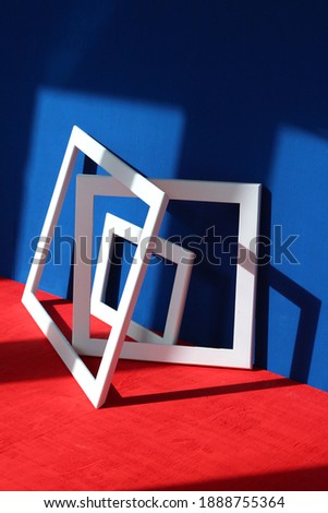 Still life: white square and rectangular frames with shadows on a blue and red background with a wooden texture. Abstract art design composition