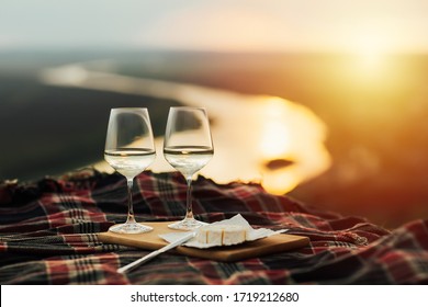 Still life. White wine and cheese. Romantic dinner outdoors at the hill with panoramic view on river. Two glasses, brie cheese on wooden tray. Amazing sunset. Copy space.
