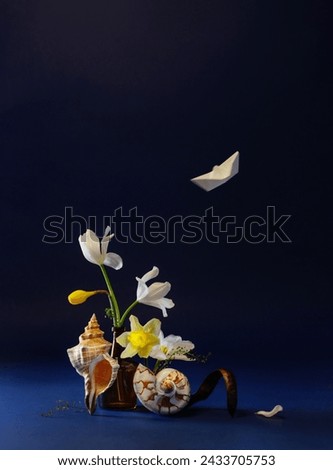 still life witn paper boat, spring flowers and  seashell  on dark blue background