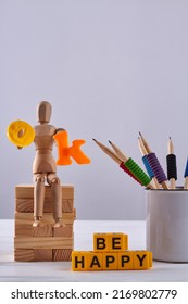 Still life wooden mannequin with cup of pencils. Yellow letter cubes arranged in be happy message.