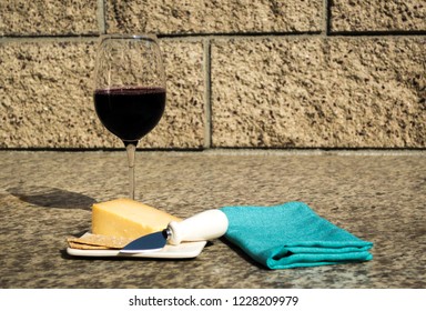 still life-glass of red wine with crackers, cheddar cheese, cheese knife on a white plate with a turquoise napkin outdoors against a stone wall - Powered by Shutterstock