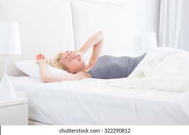 Still Sleepy And Tired Young Beautiful Woman Refuses To Wake Up And Get Of The Bad In Morning. Lack Of Sleep Concept.  Horizontal Composition