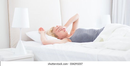 Still Sleepy And Tired Young Beautiful Woman Refuses To Wake Up And Get Of The Bad In Morning. Lack Of Sleep Concept.  Horizontal Composition.