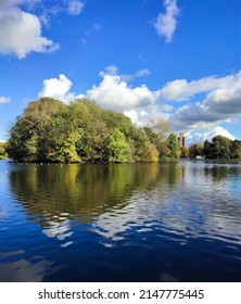 Still Water And Blue Sky With Trees And Lone Building In The Distance.