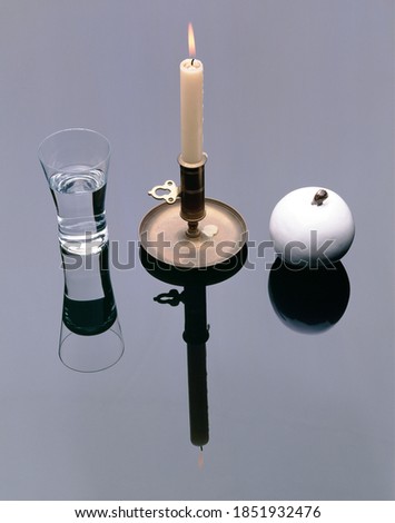 Stillife Arrangement with waterglass, holder with burning candle and white porcelain Apple on  mirror plain
