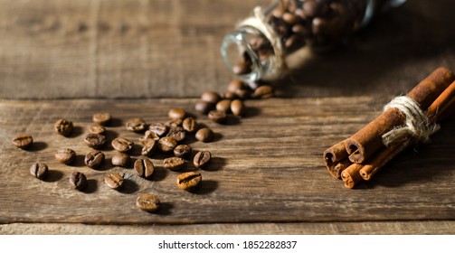 Stilllife with little bottle filled by coffee beans on the wooden background with scattered coffee beans and cinnamon
