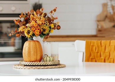 Still-life. Yellow, orange flowers in a vase, pumpkins and candles on a golden tray on a white table in a home kitchen interior. A cozy autumn concept. - Powered by Shutterstock