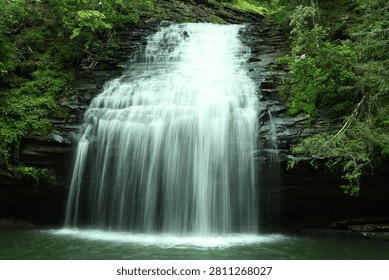 Stinging Fork Falls waterfall surrounded by lush forest in Tennessee. It's a long exposure of the falls cascading over rock formations into a peaceful pool.