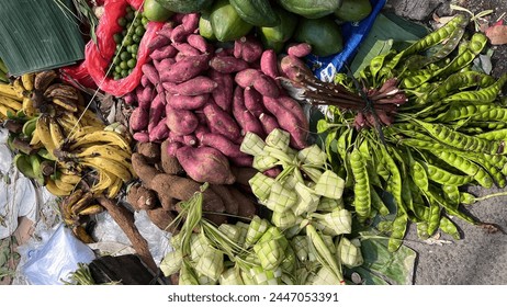 Stinky beans, sweet potatoes, cassava, bananas, kaffir lime, and woven coconut leaf pouches known as 'ketupat' are displayed on plastic mats belonging to traditional vendors in Jakarta. - Powered by Shutterstock