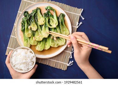 Stir Fried Bok Choy With Soy Sauce On Plate Eating With Cooked Rice By Using Chopsticks On Blue Background, Asian Vegan Food, Top View