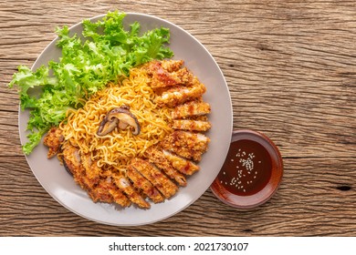 stir fried instant noodles with Japanese deep fried pork cutlet or Tonkatsu, lettuce and Shiitake mushroom beside Tonkatsu sauce topped with white sesame on rustic wood texture background, top view