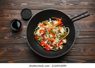 Stir fried noodles with mushrooms and vegetables in wok on wooden table, flat lay - Shutterstock ID 2124914390